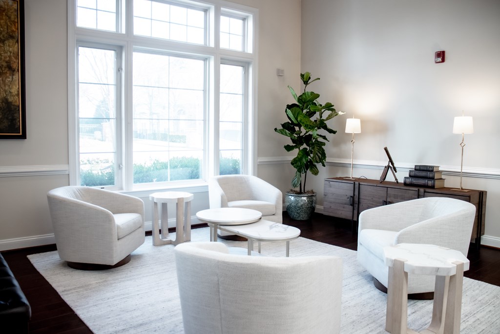 a living room with white chairs and tables and a large window at Broadlands Apartments in Ashburn, 20148